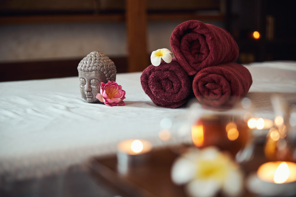 Statue of Buddha head near clean towels with flowers on couch in oriental spa center